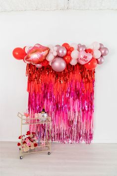 balloons and streamers are hanging on the wall next to a cart with a cake