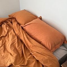 an unmade bed with orange sheets and pillows in a corner next to a night stand