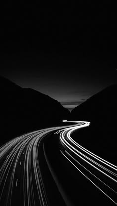 a black and white photo of a highway at night with light streaks on the road