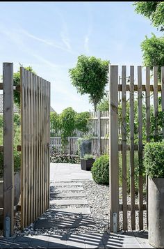 an open wooden gate in the middle of a gravel path with potted plants on either side