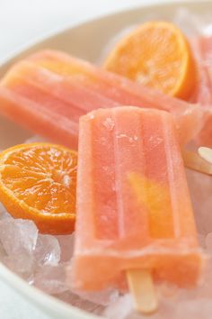 three popsicles with orange slices on top of ice in a white bowl next to an orange slice