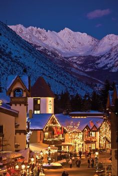 the town is lit up with christmas lights in front of mountains and snow - capped peaks