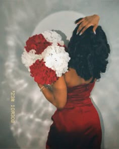 a woman in a red dress holding a bouquet of flowers on her shoulder and looking down