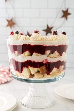 a layered cake with white frosting and raspberry topping on a glass pedestal