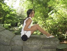 a woman sitting on top of a stone wall in the woods with her legs crossed