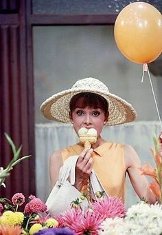 a woman in a straw hat eating an ice cream cone next to flowers and balloons