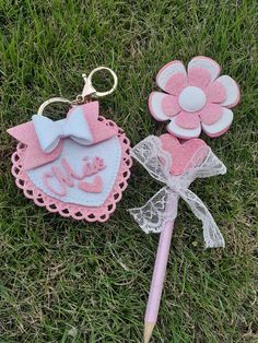 two pink and white items laying on top of the grass next to a flower keychain