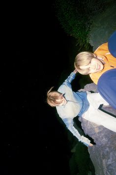 two women standing next to each other on top of a rock near the water at night