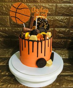 a birthday cake decorated with chocolate, candies and basketballs on a pedestal in front of a wall