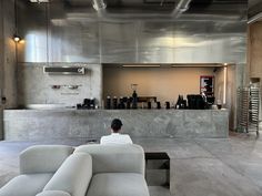 a person sitting on a couch in a room with concrete walls and flooring,