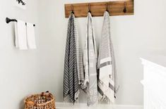 towels hanging on the wall in a white bathroom with wooden hooks and towel rack above it