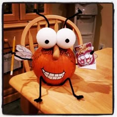 a pumpkin with googly eyes sitting on top of a table next to a pencil