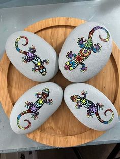 four painted rocks sitting on top of a wooden platter covered in white and multicolored geckos