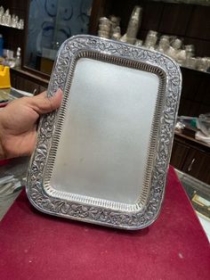 a person holding up a silver plate on top of a table