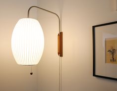 a white lamp sitting on the side of a wall next to a framed picture and an art piece