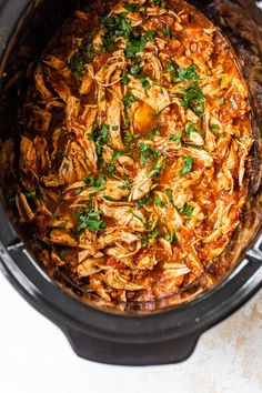 an open crock pot filled with shredded chicken and garnished with parsley