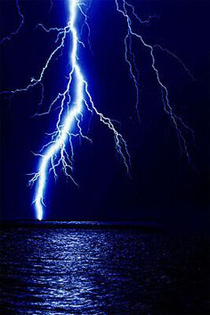 two lightning strikes over the ocean at night with bright blue lightening in the background