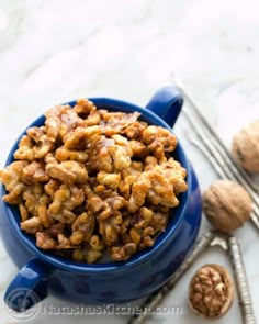 a blue bowl filled with walnuts next to two spoons and nuts on a table