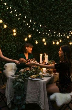 two people sitting at a table with food in front of them, surrounded by lights