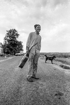 a man standing on the side of a road next to a dog and holding a briefcase