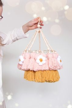 a woman holding a pink and yellow hanging decoration with white flowers on it's sides