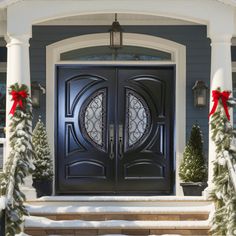 a black front door with two wreaths on the steps and snow covered trees around it