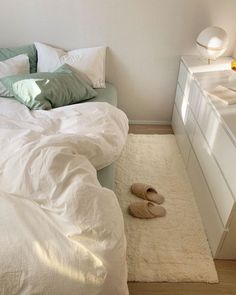 a bedroom with white bedding, green pillows and slippers on the floor next to a dresser