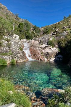 there is a small waterfall in the middle of this lake with clear blue water and green vegetation