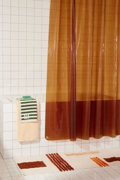 an orange and brown shower curtain next to a white tiled wall with matching rugs