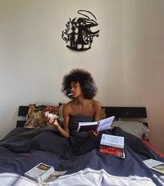 a woman sitting on top of a bed next to a wall mounted clock and reading