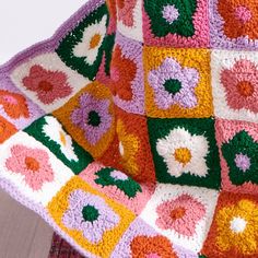 a crocheted blanket with flowers on it is sitting next to a table and chair