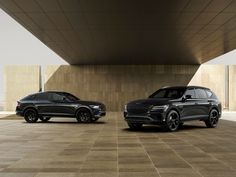 two black suvs parked next to each other in front of a large building with concrete walls