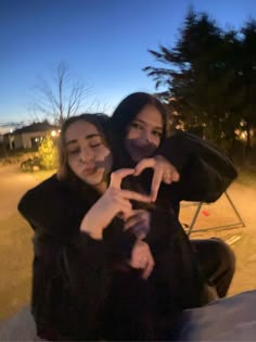 two women sitting on a bench making the shape of a heart with their hands at night