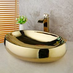 a bathroom sink that is shiny gold and has a plant in the bowl next to it