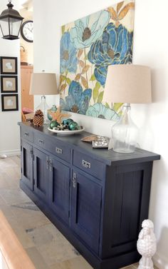 a blue buffet table with two lamps and a painting on the wall in the background