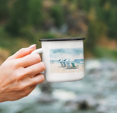 a hand holding a coffee mug with a beach scene on it