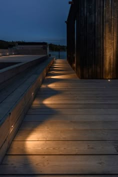 a long wooden walkway with lights on the side and dark wood building in the background