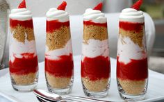 four desserts with strawberries and whipped cream in them on a white platter