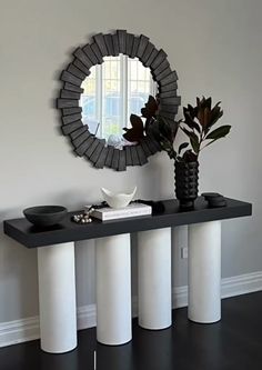 a black and white console table with two vases on it next to a round mirror