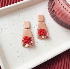 two pink earrings with flowers on them sitting on a white tray next to a vase