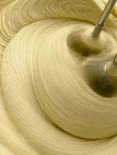 a mixing bowl filled with white cream and a metal mixer attachment in the middle of it