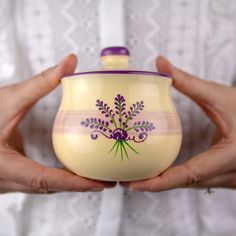 two hands holding a cream colored container with purple flowers on it