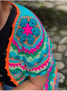 a woman wearing a colorful crocheted shawl and looking down at her cell phone