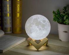 the moon lamp is sitting on top of a wooden table next to books and a potted plant