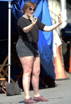 a woman in black shirt and shorts standing on street with cell phone to her ear