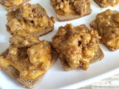 several pieces of bread topped with meat and cheese on top of each other, sitting on a white plate