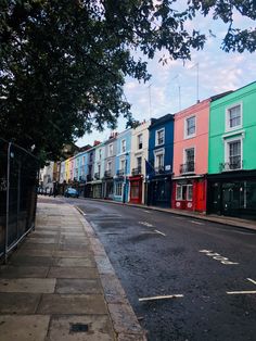 an empty street lined with multi - colored buildings on either side and trees in the foreground