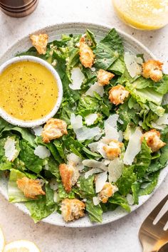 a salad on a plate with dressing and lemon wedges next to it, surrounded by utensils