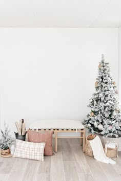 a white christmas tree with presents under it and a bench next to it in the corner