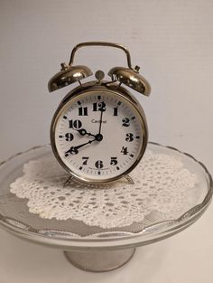 an alarm clock sitting on top of a glass cake plate with doily around it